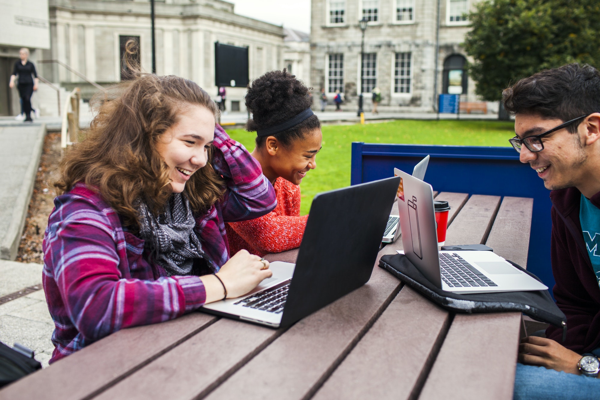 Smiling university students with laptops on table at campus