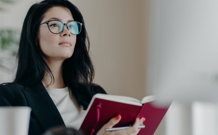 Beautiful woman with thoughtful expression, holds opened notepad, writes time management