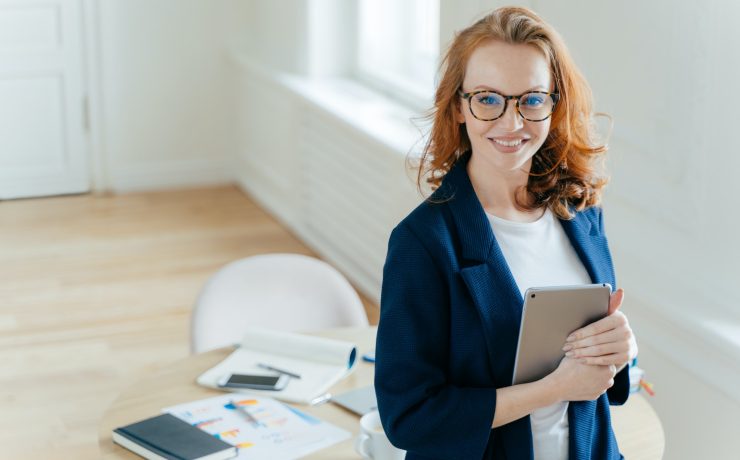 Prosperous female leader of working team holds digital tablet device, develops business ideas