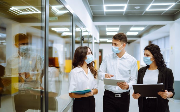 Three business colleagues in protective face mask discussing work related matters on an office.